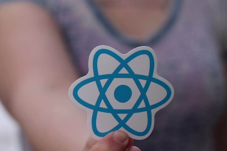 A person holding a small card with a blue and white atomic model symbol printed on it, positioned in front of their chest and partially obscuring their purple short-sleeved top. The background is blur